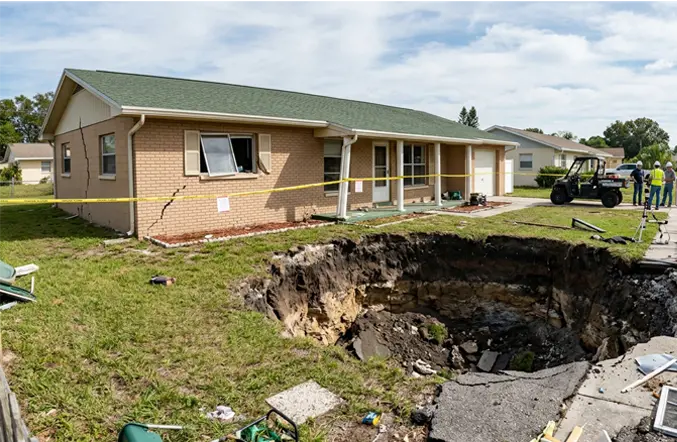 Single-story brick home in New Port Richey Florida with a massive sinkhole crater in the front lawn and caution tape